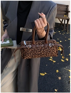 Close-up of leopard print cylinder bag with brown leather handles and buckle detail