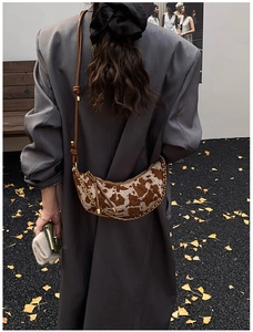 Detail of a brown cow print crescent bag with gold chain and leather strap on model