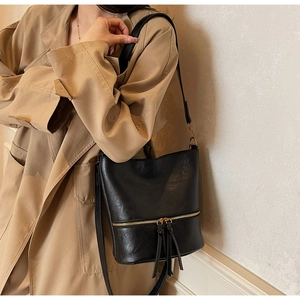 Détail du sac seau en cuir noir avec zip doré et décoration de pompon longue