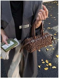 Detail of leopard print cylinder bag with brown leather handles on autumn leaf background