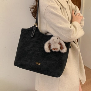 Model wearing a large black suede tote bag with gold lettering and a plush bunny charm