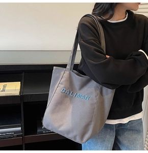 Detail of grey canvas tote bag featuring textured blue BALIMAN lettering on side