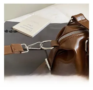 Detailed close-up of the silver metal spring hook and D-ring on a dark brown leather bag