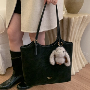 Detailed close-up of a black matte tote bag with a golden logo and plush bunny charm