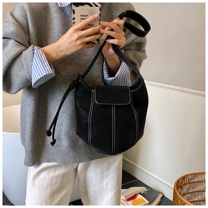 Detail of black leather bucket bag with white contrast stitching and flap closure