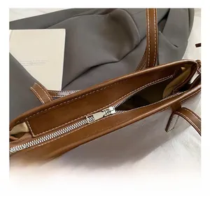 Detailed close-up of brown faux leather tote bag showing silver zipper and white stitching