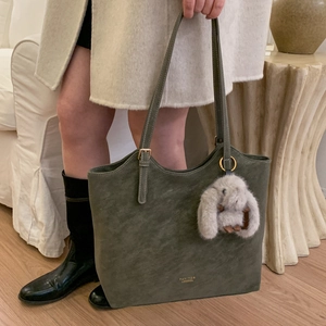 Detail view of olive green suede tote bag with golden hardware and plush rabbit charm