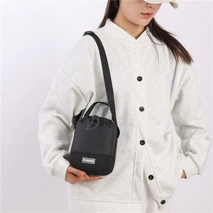Detail van zwarte mini-crossbodytas met trekkoord en modelabel gedragen op een grijs jasje