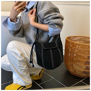 Detail of black bucket bag featuring white contrast stitching and delicate drawstring ties