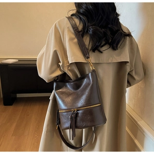 Vue détaillée du sac seau vintage en cuir marron foncé avec pompon et accents métalliques dorés
