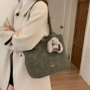 Detail of dark green matte leather tote bag with gold logo and plush rabbit pendant