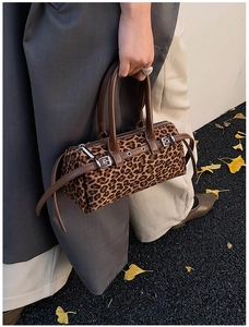 Close-up of vintage leopard print boston bag with brown leather handles and autumn leaves