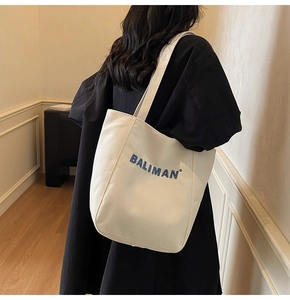 Detail of white canvas tote bag featuring blue Baliman embroidery on the shoulder strap