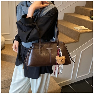 Detail of dark brown leather tote bag with contrast stitching and teddy bear charm