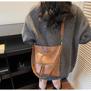 Détail d'un sac seau vintage marron avec fermetures éclair et pompons en cuir sur modèle