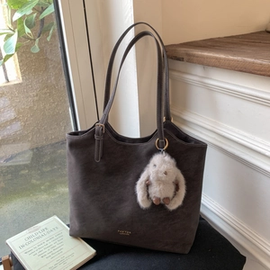 Detail of taupe suede tote bag featuring a cute plush rabbit charm and vintage book
