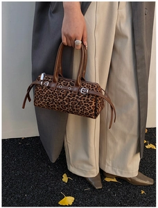 Detail of leopard print cylindrical bag with leather handles held by a model in autumn