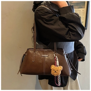Detail of dark brown leather tote featuring white stitching and a yellow plush bear charm