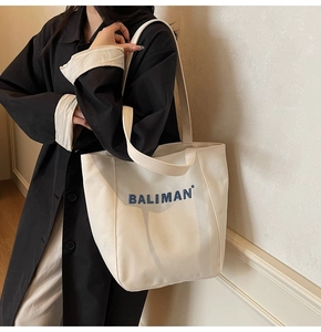 Detail view of a white canvas tote bag with blue text print on a model's shoulder