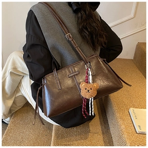 Detail of vintage brown leather tote bag with white stitching and plush bear charm