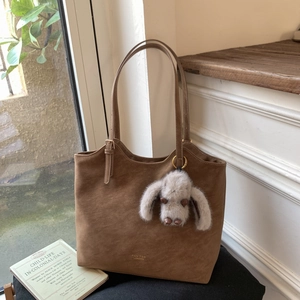 Detail of vintage brown suede tote bag with gold logo lettering and a plush animal charm