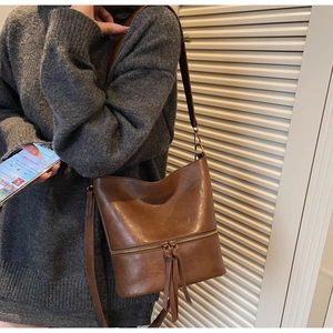 Détails du sac seau vintage marron avec pompons et poche zippée sur un pull gris chiné