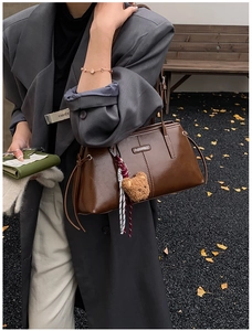 Detail of dark brown glossy leather tote bag with a cute plush bear charm and metallic logo