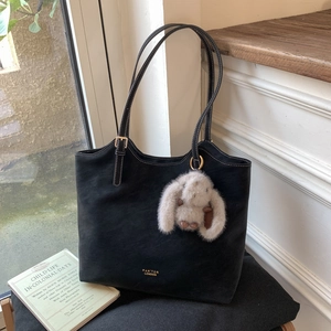 Close-up of black suede tote bag with white stitching and plush rabbit charm detail