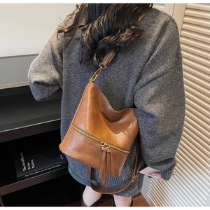 Détail d'un sac seau vintage marron avec fermeture éclair à pompons porté par un mannequin