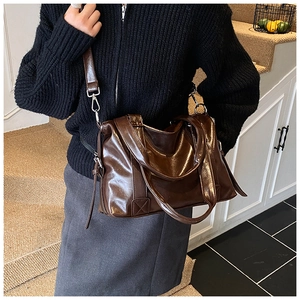 Detailed view of deep brown large tote bag with shiny oil wax leather texture worn by model