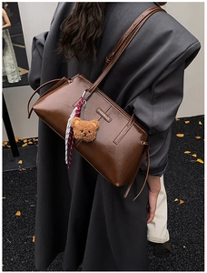 Detail view of deep brown faux leather tote bag with white stitching and bear charm accessory