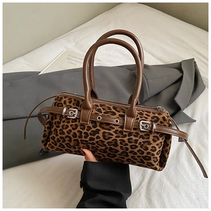 Close-up of leopard print handbag with leather straps and metal hardware on white fabric