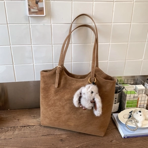 Vintage brown faux suede tote bag with plush bunny charm on a wooden desk setup