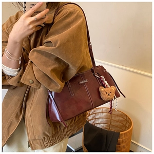 Detail of burgundy leather tote bag with white stitching and plush bear charm on model