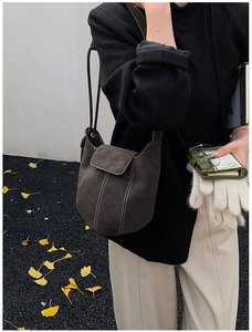 Detail of dark grey suede bucket bag with contrast stitching on autumn leaves background