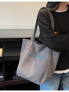 Grey canvas tote bag with BALIMAN blue embroidery shown worn on a model's shoulder