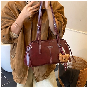 Detailed close-up of wine red faux leather tote bag with metallic emblem and bear charm