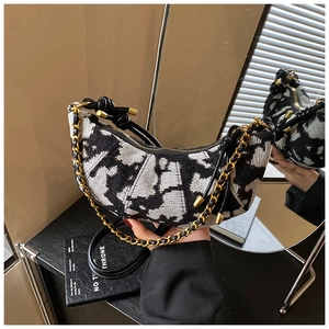 Detail of half-moon shoulder bag featuring black and white abstract knit pattern and gold chain