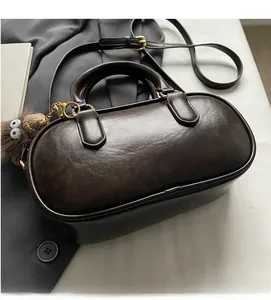 Details einer kaffeebraunen Bowling-Tasche mit goldenem Reißverschluss und Anhänger
