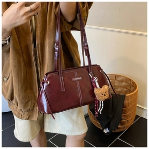 Detail view of burgundy leather tote bag with white stitching and bear charm
