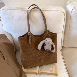 Brown suede tote bag with adjustable strap and cute rabbit pendant on white sofa