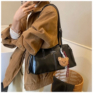 Close-up of black PU leather handbag featuring white contrast stitching and a bear pendant
