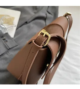 Close-up of brown litchi grain leather shoulder bag with adjustable gold buckle detail