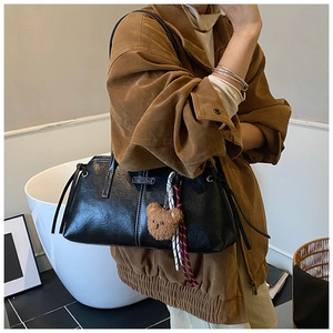 Detail of black glossy PU leather shoulder bag featuring side drawstring and metal nameplate