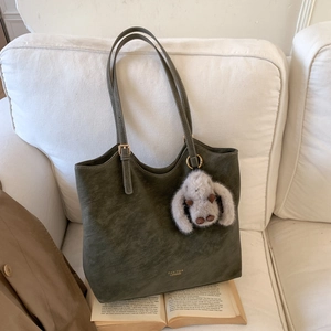 Detail of olive green suede tote bag with plush rabbit charm on a white fabric sofa