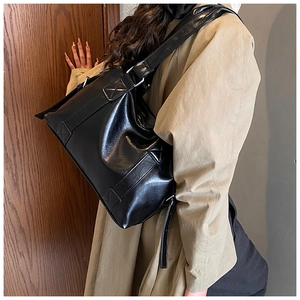 Close-up of black glossy leather tote bag with wide shoulder strap and cross stitching