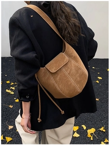 Close-up of brown suede bucket bag with curved design and autumn ginkgo leaf background