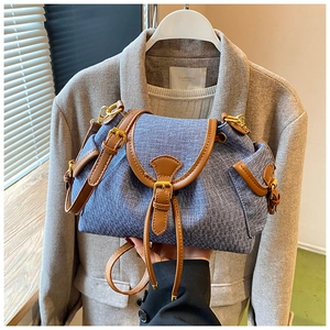 Detail of blue denim bucket bag featuring brown leather trim and gold metal hardware