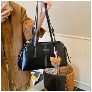 Detail of black leather tote bag with white contrast stitching and a plush bear charm