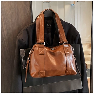 Detail of a brown polished leather tote bag showing the texture and metal hardware buckle